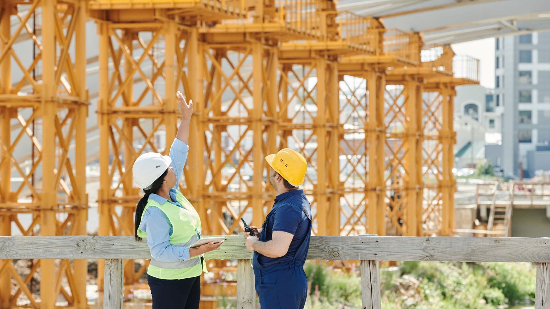 Two engineers in hardhats discuss projects at a busy construction site.