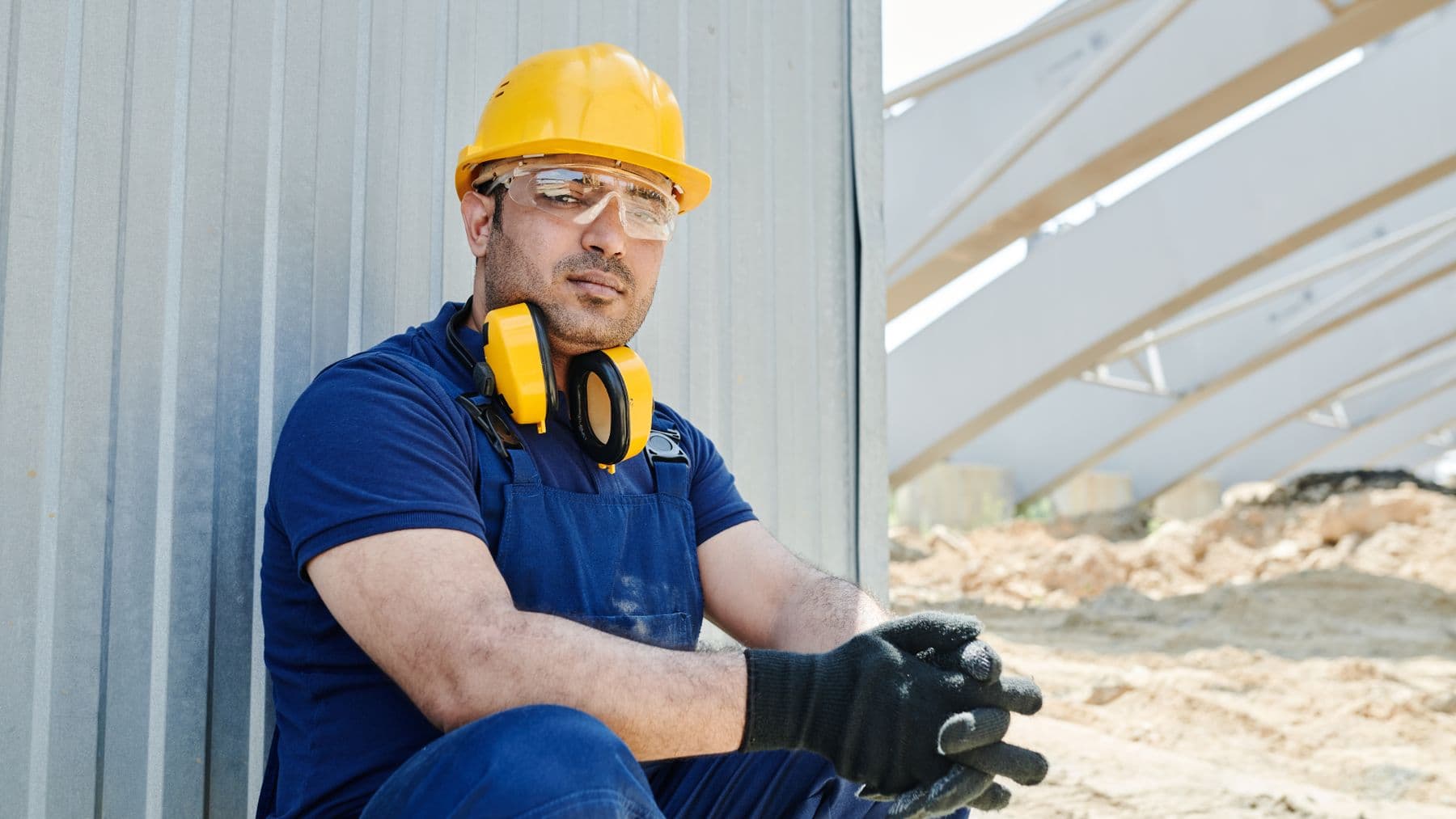 A male construction worker wearing safety gear sits at a construction site, showcasing standard industry protection.